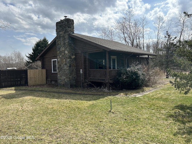 view of side of home with a yard, covered porch, a chimney, and fence