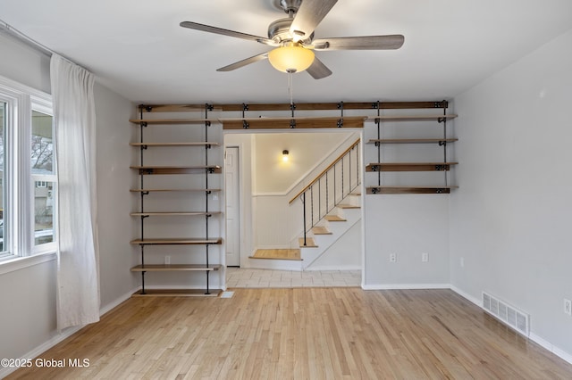 unfurnished room featuring ceiling fan, visible vents, stairway, wood finished floors, and baseboards