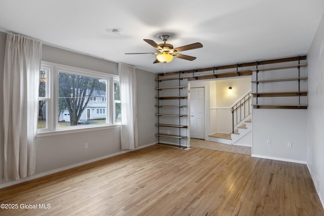 unfurnished room featuring stairway, wood-type flooring, baseboards, and ceiling fan
