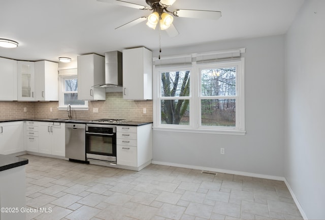 kitchen with backsplash, dark countertops, wall chimney exhaust hood, appliances with stainless steel finishes, and a sink