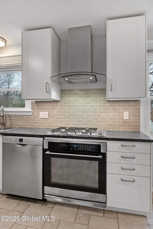 kitchen with white cabinets, wall chimney exhaust hood, backsplash, and appliances with stainless steel finishes
