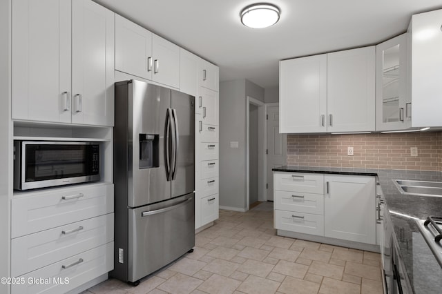 kitchen with glass insert cabinets, white cabinets, a sink, appliances with stainless steel finishes, and backsplash