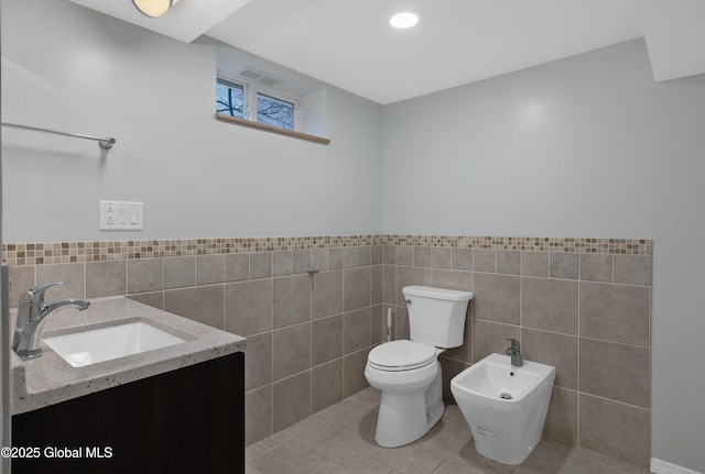 bathroom featuring a bidet, vanity, tile patterned flooring, toilet, and tile walls