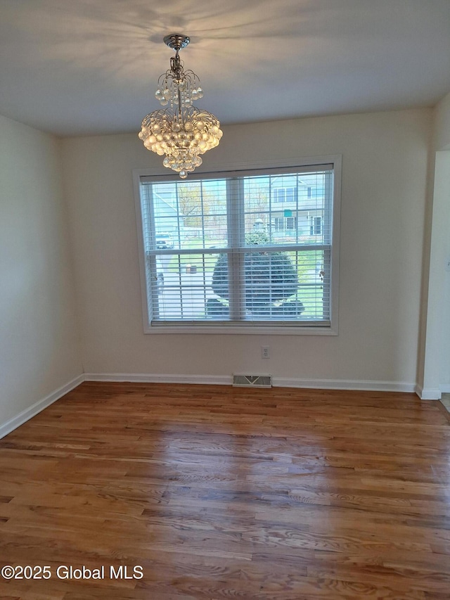 unfurnished dining area with visible vents, baseboards, wood finished floors, and a notable chandelier