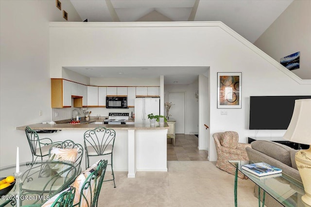 kitchen with a sink, black microwave, electric range oven, a peninsula, and freestanding refrigerator