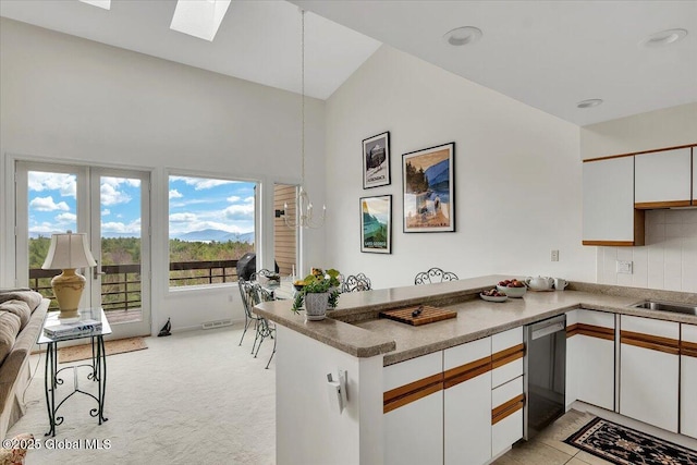 kitchen with high vaulted ceiling, a skylight, white cabinets, a peninsula, and dishwashing machine
