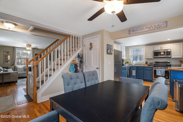 dining space with plenty of natural light, light wood finished floors, ceiling fan, and stairs