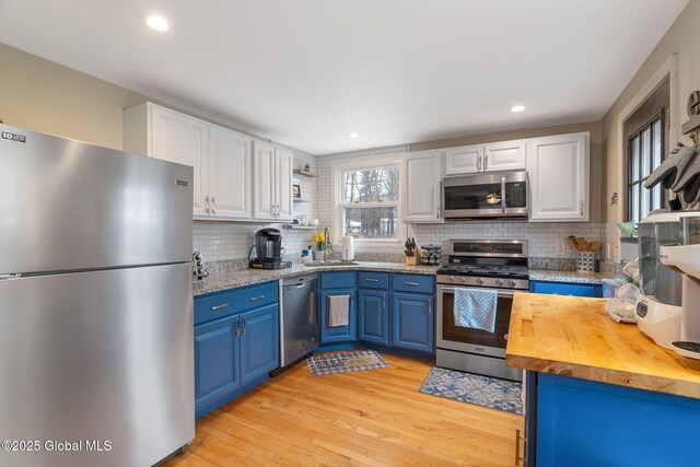 kitchen with white cabinets, blue cabinetry, stainless steel appliances, backsplash, and butcher block counters