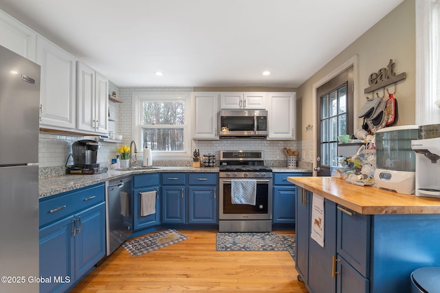 kitchen featuring blue cabinets, appliances with stainless steel finishes, a sink, wood counters, and white cabinetry
