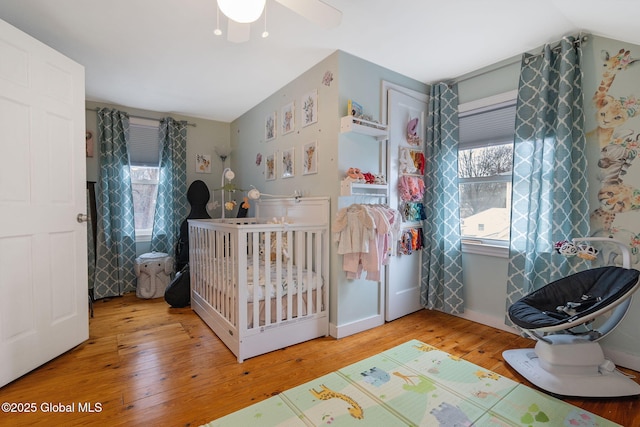 bedroom featuring a nursery area, hardwood / wood-style floors, and lofted ceiling
