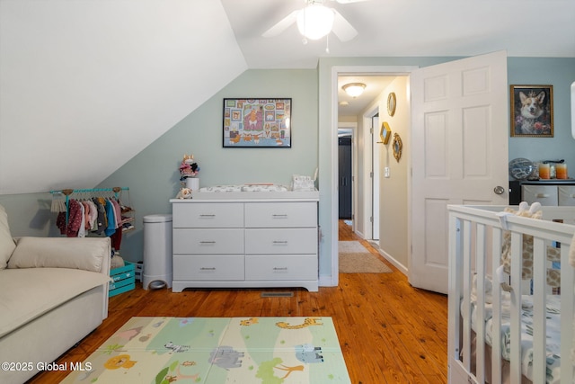bedroom featuring a crib, ceiling fan, wood finished floors, and vaulted ceiling