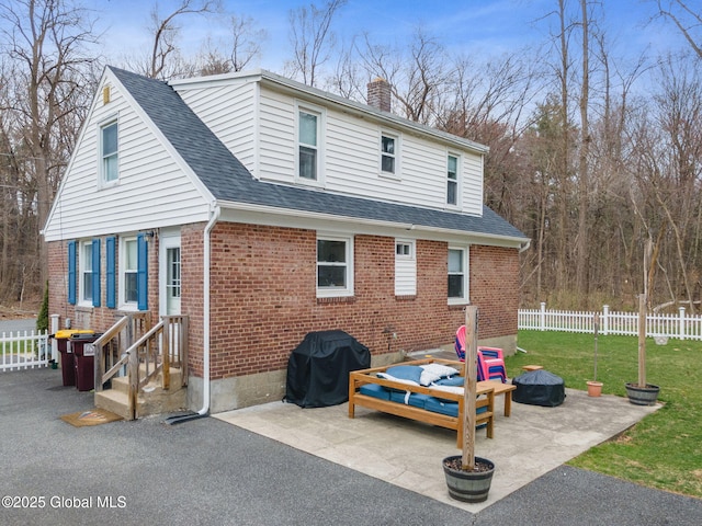 rear view of house featuring brick siding, a patio, fence, and a chimney