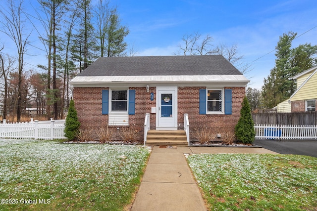 bungalow-style house featuring fence, a shingled roof, a front lawn, and brick siding