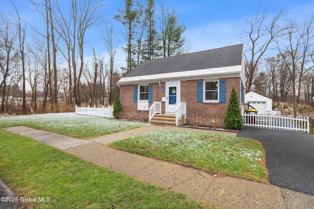 view of front of home with an outbuilding, a detached garage, brick siding, fence, and a front lawn