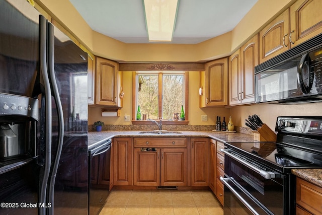 kitchen with brown cabinetry, a sink, light tile patterned floors, and black appliances