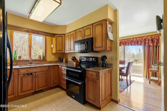 kitchen featuring a sink, brown cabinetry, dark stone countertops, light tile patterned floors, and black appliances