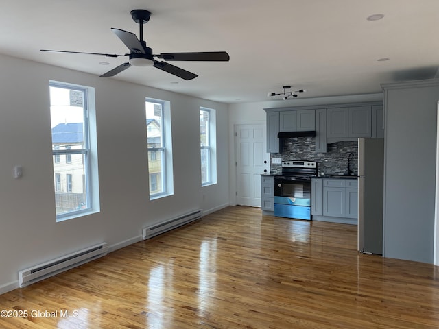 unfurnished living room with light wood finished floors, a baseboard heating unit, and ceiling fan