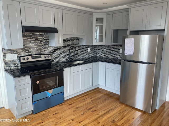 kitchen featuring a sink, freestanding refrigerator, under cabinet range hood, range with electric cooktop, and dark countertops