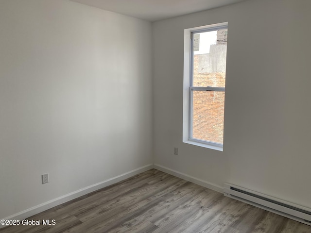 empty room featuring baseboards, a baseboard heating unit, and wood finished floors