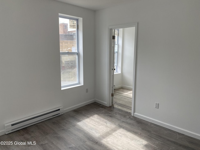 spare room featuring baseboards, a baseboard heating unit, and wood finished floors