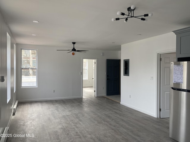 unfurnished living room with baseboards, a wealth of natural light, wood finished floors, and ceiling fan with notable chandelier