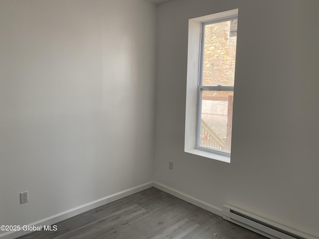 spare room featuring baseboards, wood finished floors, and a baseboard heating unit