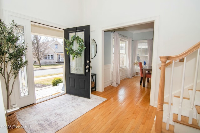 entryway featuring a decorative wall, light wood finished floors, stairs, ornamental molding, and wainscoting