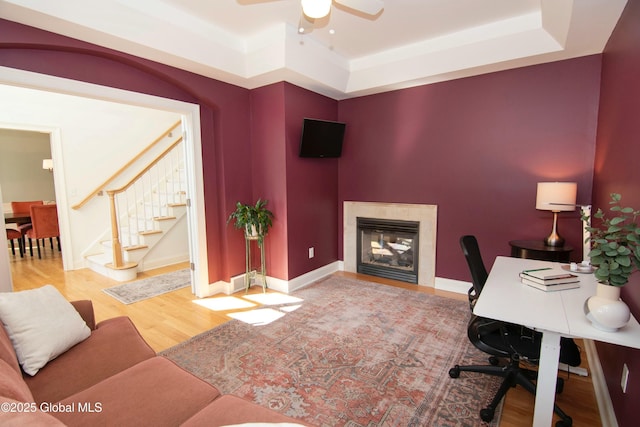 office space with ceiling fan, a tray ceiling, a glass covered fireplace, and wood finished floors