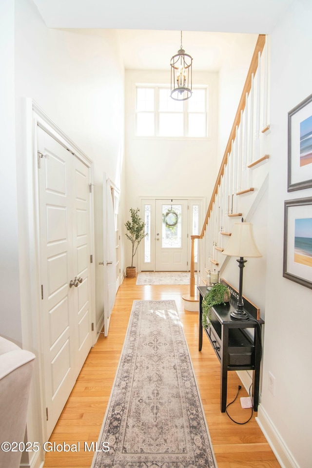 entryway featuring light wood finished floors, baseboards, stairway, a high ceiling, and a notable chandelier