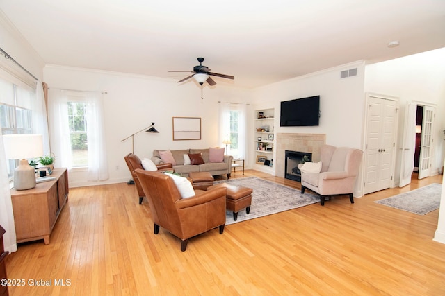 living area featuring light wood-style flooring, ornamental molding, a fireplace, and visible vents