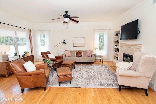 living room with a tiled fireplace, wood finished floors, ornamental molding, and a ceiling fan