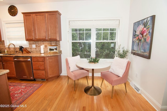 kitchen with a sink, light wood finished floors, stainless steel dishwasher, brown cabinetry, and decorative backsplash