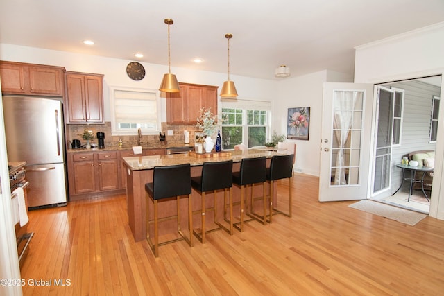 kitchen with brown cabinetry, light wood-style flooring, decorative backsplash, and stainless steel appliances