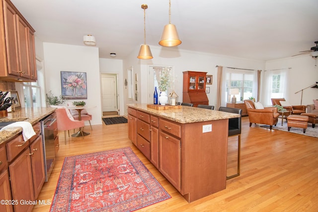 kitchen featuring open floor plan, a breakfast bar, light wood finished floors, pendant lighting, and brown cabinets