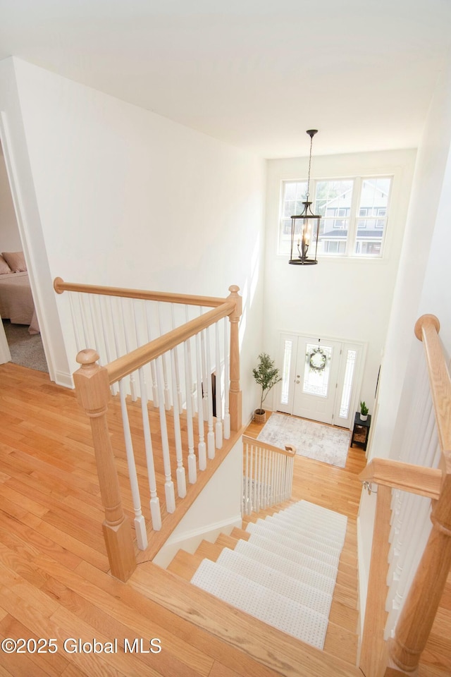 stairs featuring a high ceiling, a wealth of natural light, wood finished floors, and a notable chandelier