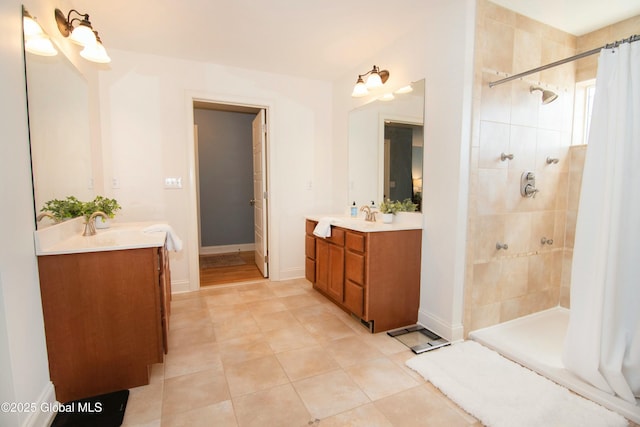 bathroom with baseboards, tile patterned floors, a sink, two vanities, and tiled shower