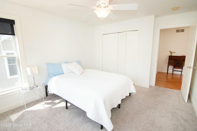 carpeted bedroom with a closet, baseboards, visible vents, and a ceiling fan
