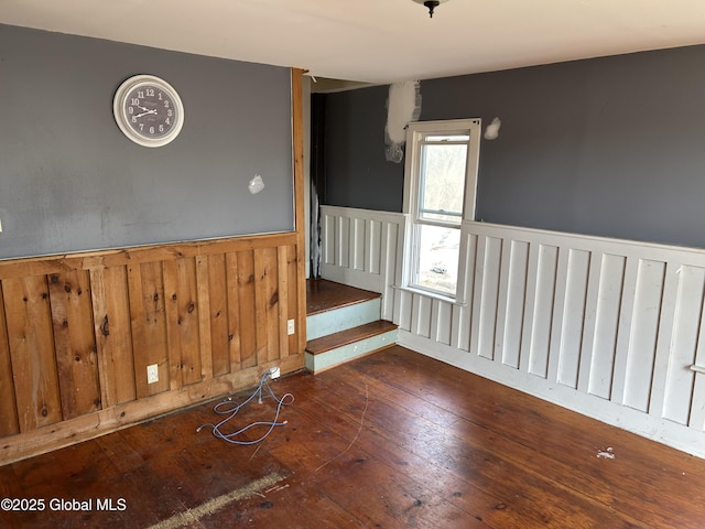 unfurnished room featuring hardwood / wood-style floors, stairway, and wainscoting