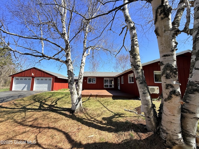 ranch-style home with aphalt driveway, a garage, board and batten siding, a front yard, and an outdoor structure