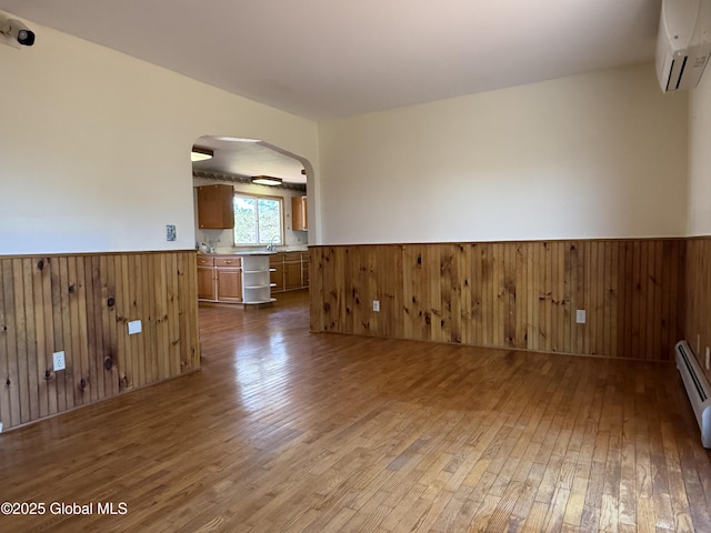 spare room with arched walkways, wood-type flooring, wainscoting, and a wall mounted AC