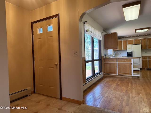 kitchen with arched walkways, white refrigerator with ice dispenser, baseboard heating, and baseboards