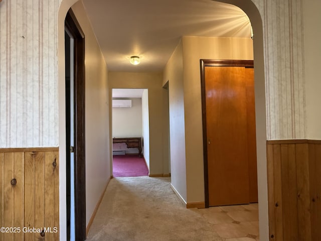 hall featuring arched walkways, baseboards, a wall unit AC, and carpet floors