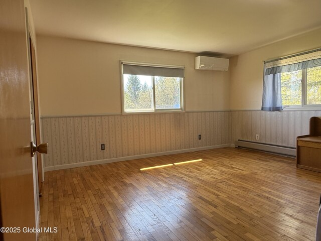 spare room with baseboard heating, wainscoting, hardwood / wood-style floors, and an AC wall unit