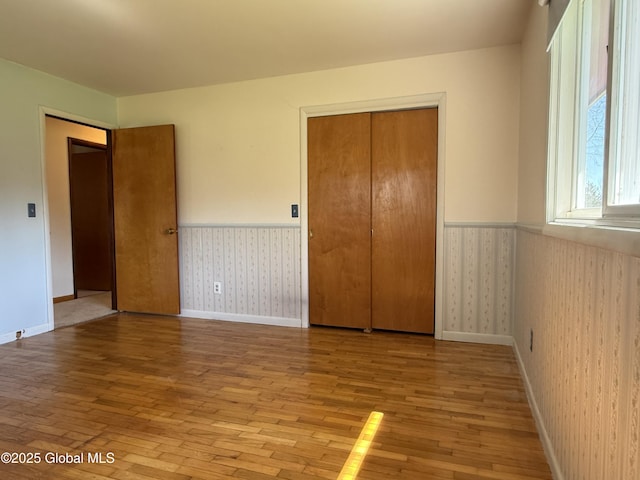 unfurnished bedroom with wallpapered walls, a wainscoted wall, light wood finished floors, and a closet