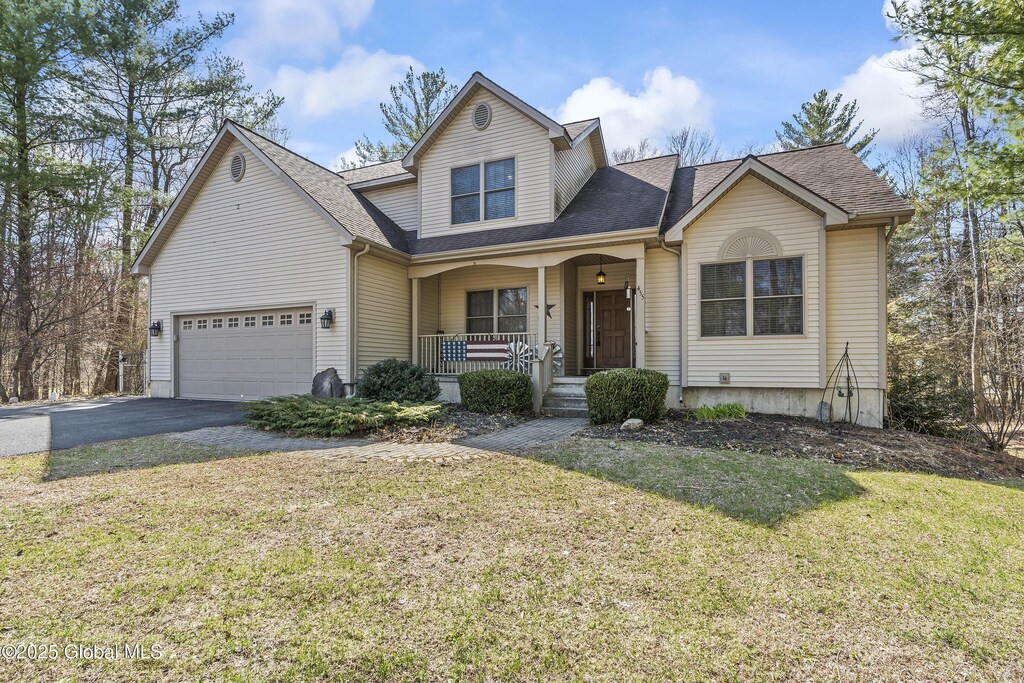 traditional-style house featuring a front lawn, aphalt driveway, a shingled roof, covered porch, and an attached garage