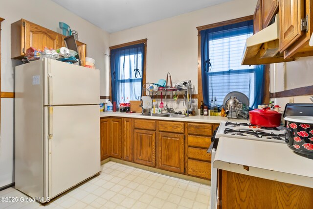 kitchen with light countertops, a sink, light floors, brown cabinetry, and white appliances