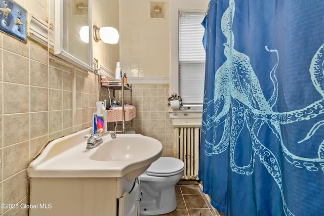 full bathroom featuring tile patterned floors, toilet, radiator, visible vents, and tile walls