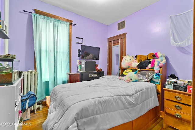 bedroom with visible vents, radiator heating unit, and wood finished floors