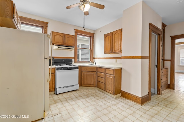 kitchen featuring range hood, white appliances, ceiling fan, brown cabinets, and a sink
