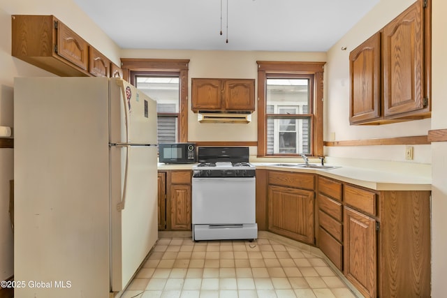 kitchen with under cabinet range hood, a sink, brown cabinets, and white appliances